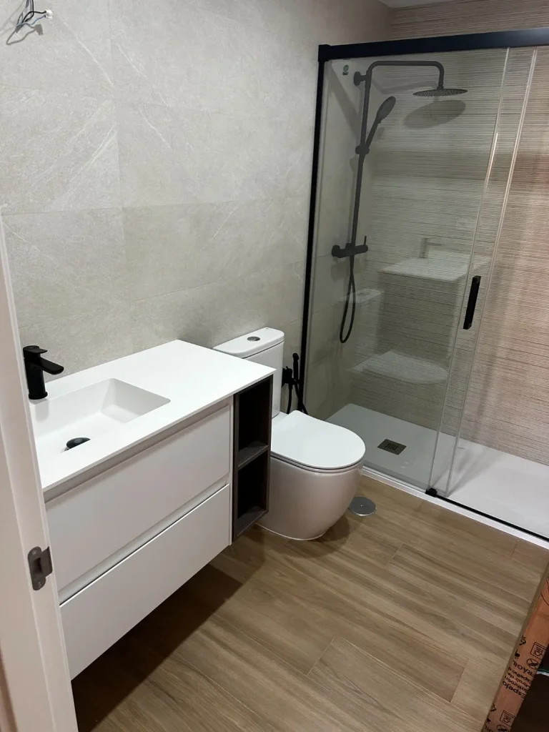 Baño terminado con mampara negra y mueble blanco a medida